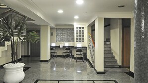 A lobby with a polished floor, a reception desk, a staircase, and a wall with framed pictures. - Plaza Inn San Conrado (Goiânia)