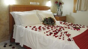 A neatly made bed with white linens and red rose petals scattered across it. - Plaza Inn San Conrado (Goiânia)