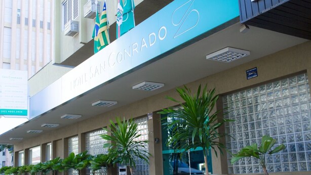 The exterior of the San Concordo hotel with a prominent sign, large windows, and potted plants in front. - Plaza Inn San Conrado (Goiânia)