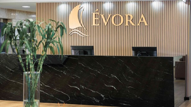 A reception desk with a logo, a plant, and a black marble counter. - Evora Hotel (Florianópolis)