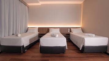 A hotel room with three single beds, a wooden floor, and a large window with curtains.