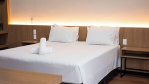 A hotel room with a large bed, two bedside tables, and a wall-mounted light. - Evora Hotel (Florianópolis)