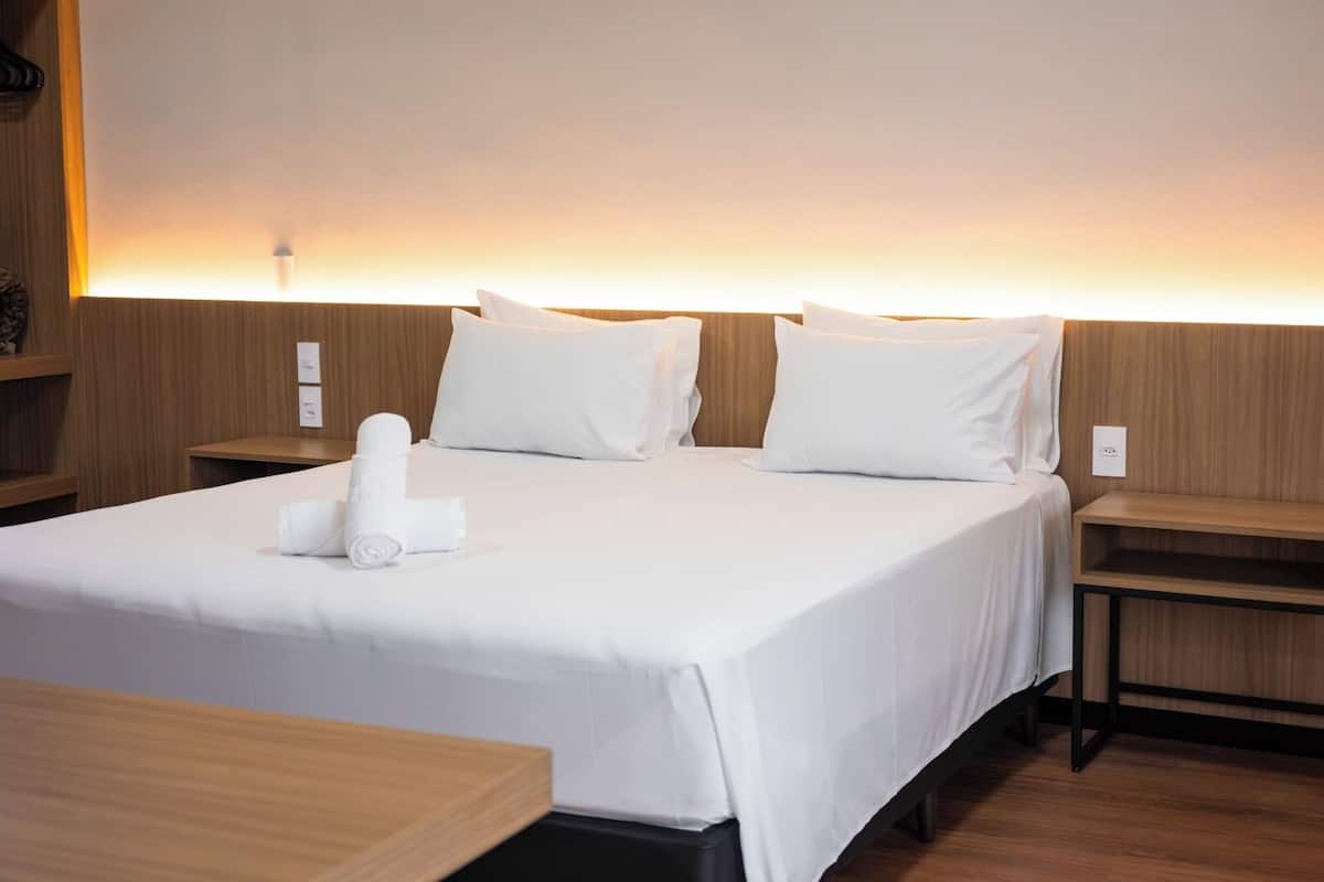 Habitación de hotel con una cama grande, dos mesitas de noche y una lámpara fijada a la pared.
