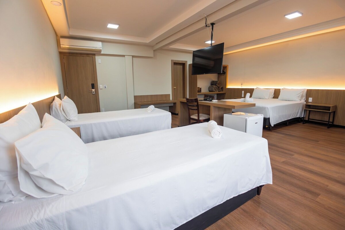 A hotel room with two beds, a desk, a TV, and a kitchenette.