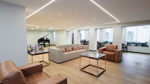 A spacious living room with a piano, leather sofas, and a glass coffee table. - Evora Hotel (Florianópolis)