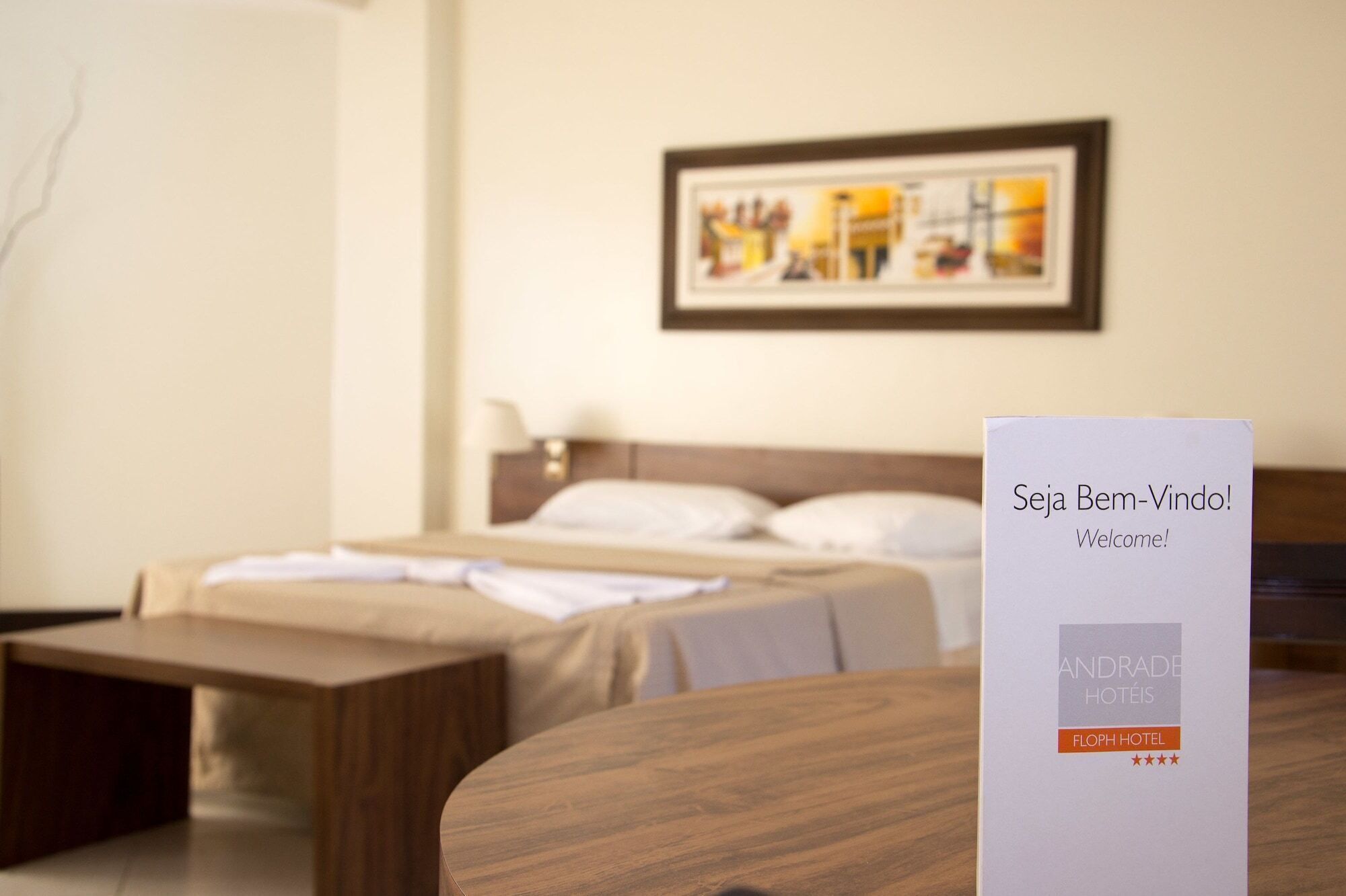 Una habitación de hotel con una cama, un banco de madera y un cartel de bienvenida.