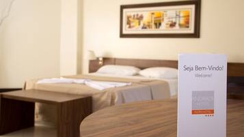 Una habitación de hotel con una cama, un banco de madera y un cartel de bienvenida.