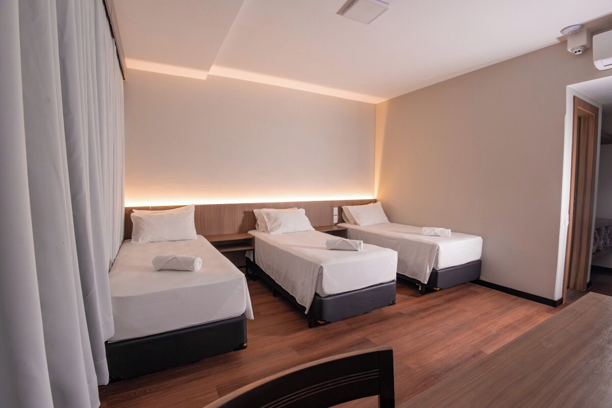 A hotel room with two beds, a wooden floor, and a large window.