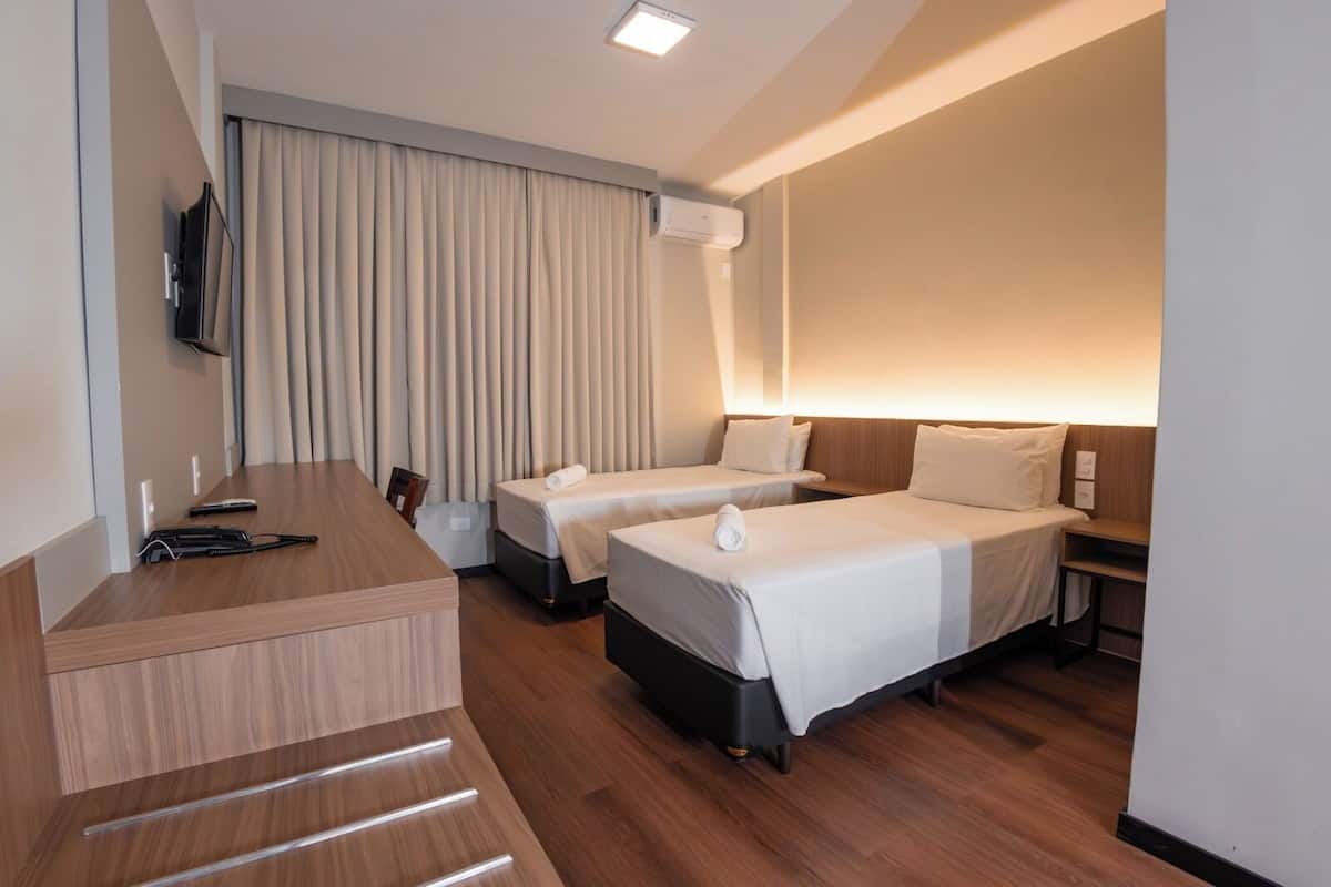 Habitación de hotel con dos camas, un escritorio, un televisor y un aire acondicionado.