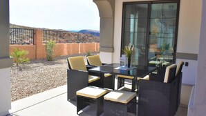 An outdoor patio with a glass table and wicker chairs, a small plant, and a view of the desert landscape. - 5 Bedroom & 5 Bathrooms Beautiful Washington Home. YEAR ROUND Pool access (Washington)