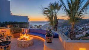A rooftop terrace with a fire pit, seating area, and potted plants.