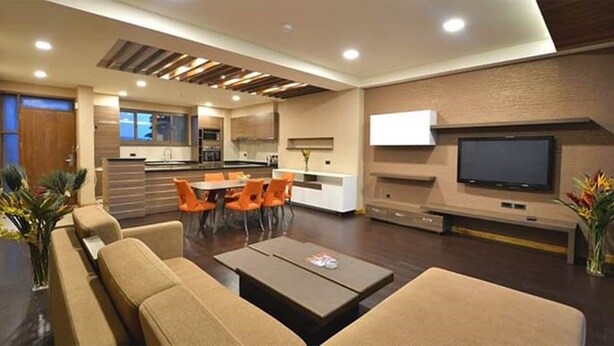 A modern living room with a sofa, coffee table, and orange chairs. There is a kitchen area with a dining table and chairs, and a flat-screen TV mounted on the wall. - Perfect place to stay wail you are in Kampala (Kampala)