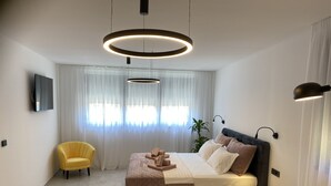 A modern bedroom with a bed, a yellow armchair, a black armchair, a TV, and a plant. - LuxuriousVilla , sauna, sea view, 200 m from the beach (Fažana)