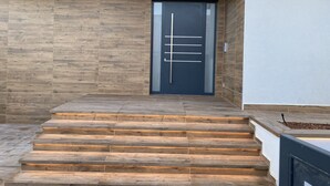 A modern building entrance with a dark door, wooden steps, and a light-colored wall. - LuxuriousVilla , sauna, sea view, 200 m from the beach (Fažana)