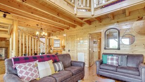 A wooden cabin interior with two sofas, a dining area, and a loft space. - 'Mountain Dreams' Cabin: Hot Tub, Sauna & Views! (Sevierville)