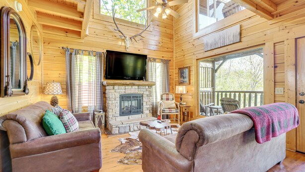 A cozy cabin interior with a stone fireplace, wooden furniture, and a television. - 'Mountain Dreams' Cabin: Hot Tub, Sauna & Views! (Sevierville)