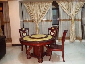 A dining area with a round table and four chairs, a large window with curtains, and a tiled floor. - Go around Kampala all day to return to your wonderful apartment (Kampala)