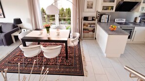 A modern kitchen with white cabinetry, a dining area with a table and chairs, and a view of greenery outside.