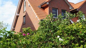 A red-tiled roof house with a brick exterior, surrounded by green foliage and flowers.