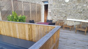 A wooden deck with a built-in seating area, a stone wall, and a door leading to an interior space.
