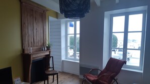 A living room with a wooden cabinet, a rocking chair, a fireplace, and large windows.