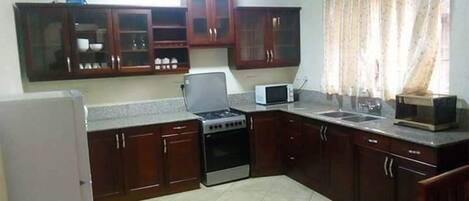 A compact kitchen with dark wooden cabinets, a built-in microwave, a stove, and a refrigerator.