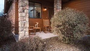 Une cabane en bois avec un porche en pierre, deux chaises en bois et une petite table.