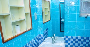 A bathroom with blue and white checkered tiles, a white sink with a faucet, and a mirror above the sink. - Sirona Getaway Hotel (Nairobi)