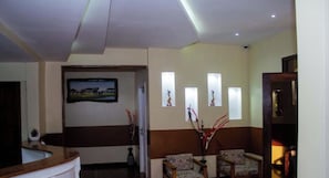 A reception area with a reception desk, two patterned armchairs, a painting, and three wall-mounted light fixtures.