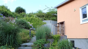 Una casa con una scala in pietra che conduce a una porta, immersa nel verde e circondata da piante fiorite.