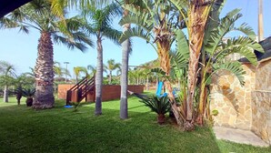A well-maintained garden with palm trees, a hammock, and a stone wall. - Villa Solemare Verde Privat Pool. (Balestrate, Sizilien)