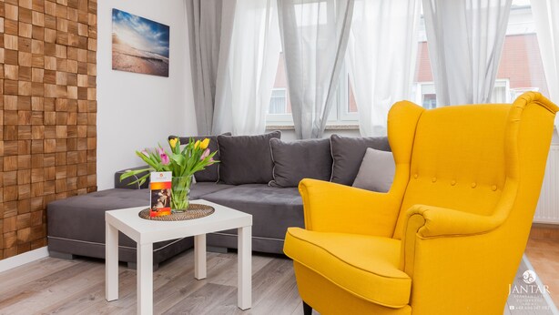 Un moderno salón con un sofá gris, un sillón amarillo, una mesa de centro blanca con un jarrón de flores y un panel de pared de madera.
