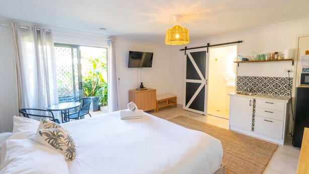 Une chambre d’hôtel équipée d’un lit, d’un bureau, d’une télévision, d’une kitchenette et d’une porte coulissante donnant sur un balcon.