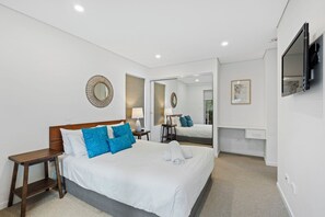 Ein Hotelzimmer mit einem großen Bett, Nachttischen, einem Spiegel, einem Fernseher und einem durch eine offene Tür einsehbaren Badezimmer.