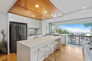 Una cocina moderna con una isla central, taburetes de bar y vistas al océano.