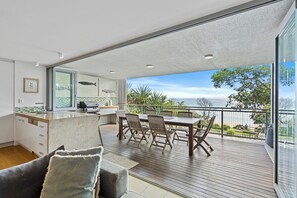 Eine moderne Küche mit Meerblick, ein Essbereich mit Holzmöbeln und ein Balkon mit Geländer.