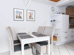 Un comedor con una mesa blanca y sillas de mimbre, una obra de arte enmarcada en la pared y un armario blanco con estantes.