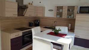 A modern kitchen with wooden cabinets, a built-in oven, a coffee maker, and a dining area with a white table and chairs. - Holiday house Fichtenwalde, 160m², 2.5 BZ, 3SZ, WZ, dining room, kitchen, garden, VDSL (Beelitz)