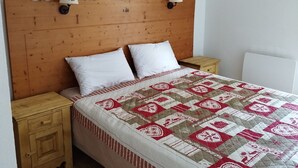 Una cama con colcha, dos almohadas blancas, cabecera de madera, dos mesitas de noche y dos lámparas fijadas a la pared.
