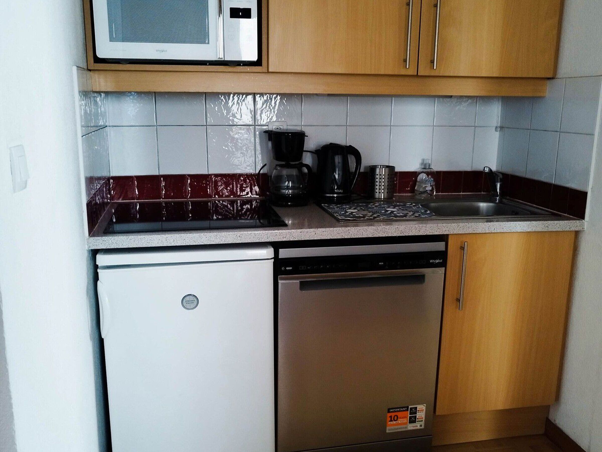 Ett kompakt kök med mikrovågsugn, kaffebryggare, vattenkokare och diskmaskin.
