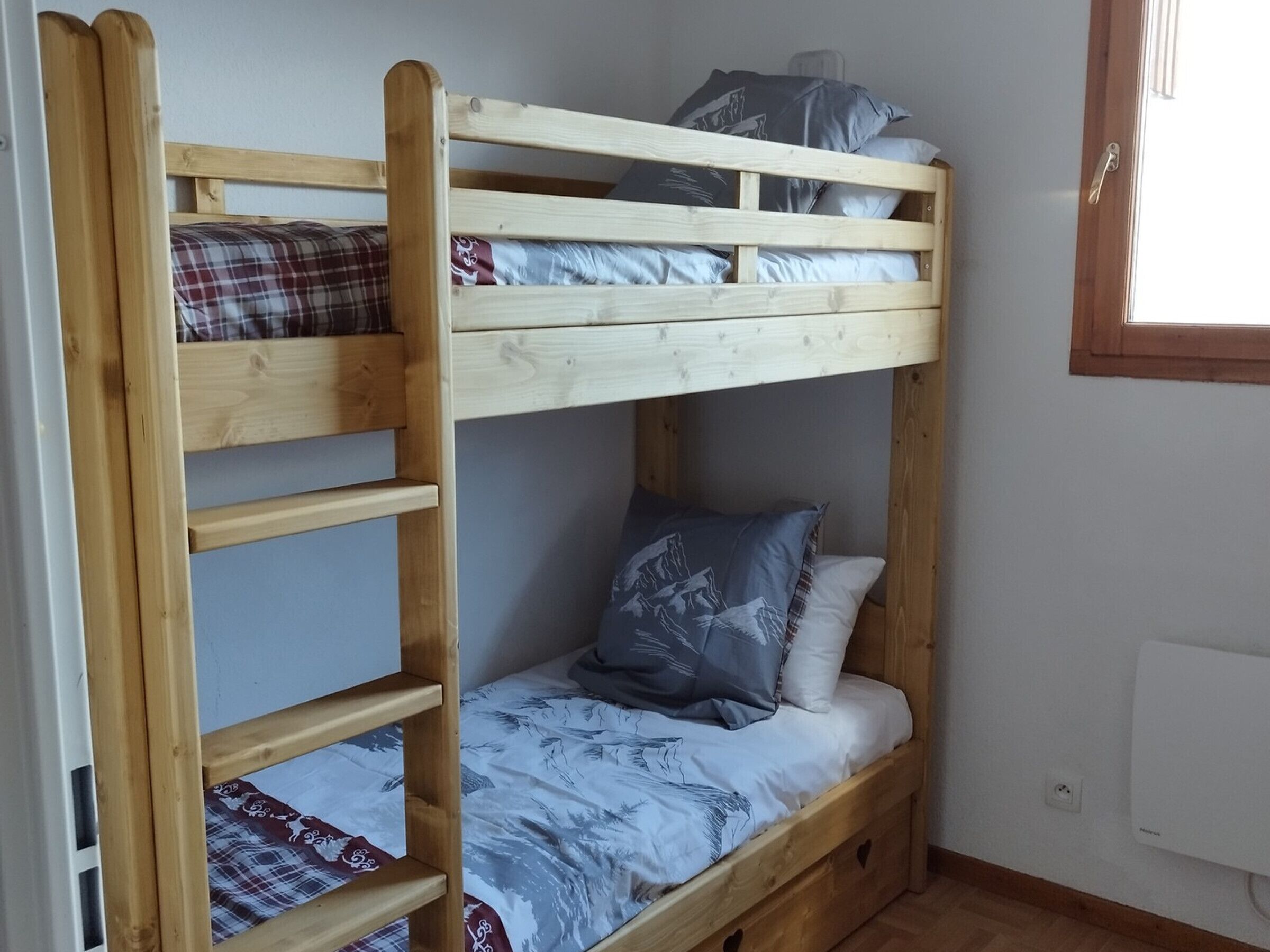 Una cama litera con escalera, una ventana y un enchufe en la pared.