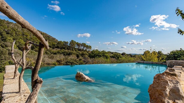 Ein klares, blaues Schwimmbecken mit natürlichen Felsformationen und Bäumen im Hintergrund.