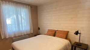 A bedroom with a large bed, two pillows, a nightstand with a lamp, and a window with sheer curtains. - Le Petit Paradis Provençal (Cigales 2) (Allemagne en Provence)