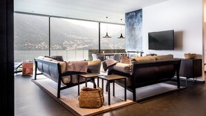 A modern living room with a large window overlooking a scenic view, a flat-screen TV mounted on the wall, and contemporary furniture. - Marvelous Lake Destination eco-friendly villa (Brienno)