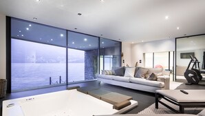 A modern living room with a large window, a sofa, a massage table, and an exercise bike. - Marvelous Lake Destination eco-friendly villa (Brienno)