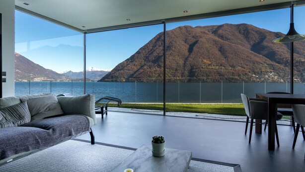 A modern living room with a large window overlooking a lake and mountains. - Marvelous Lake Destination eco-friendly villa (Brienno)