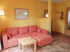A living room with a pink sofa, a wooden coffee table, a map on the wall, and a mirror on the door.