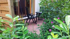 Eine Terrasse mit Tisch und Stühlen, umgeben von üppigem Grün und blühenden Pflanzen.