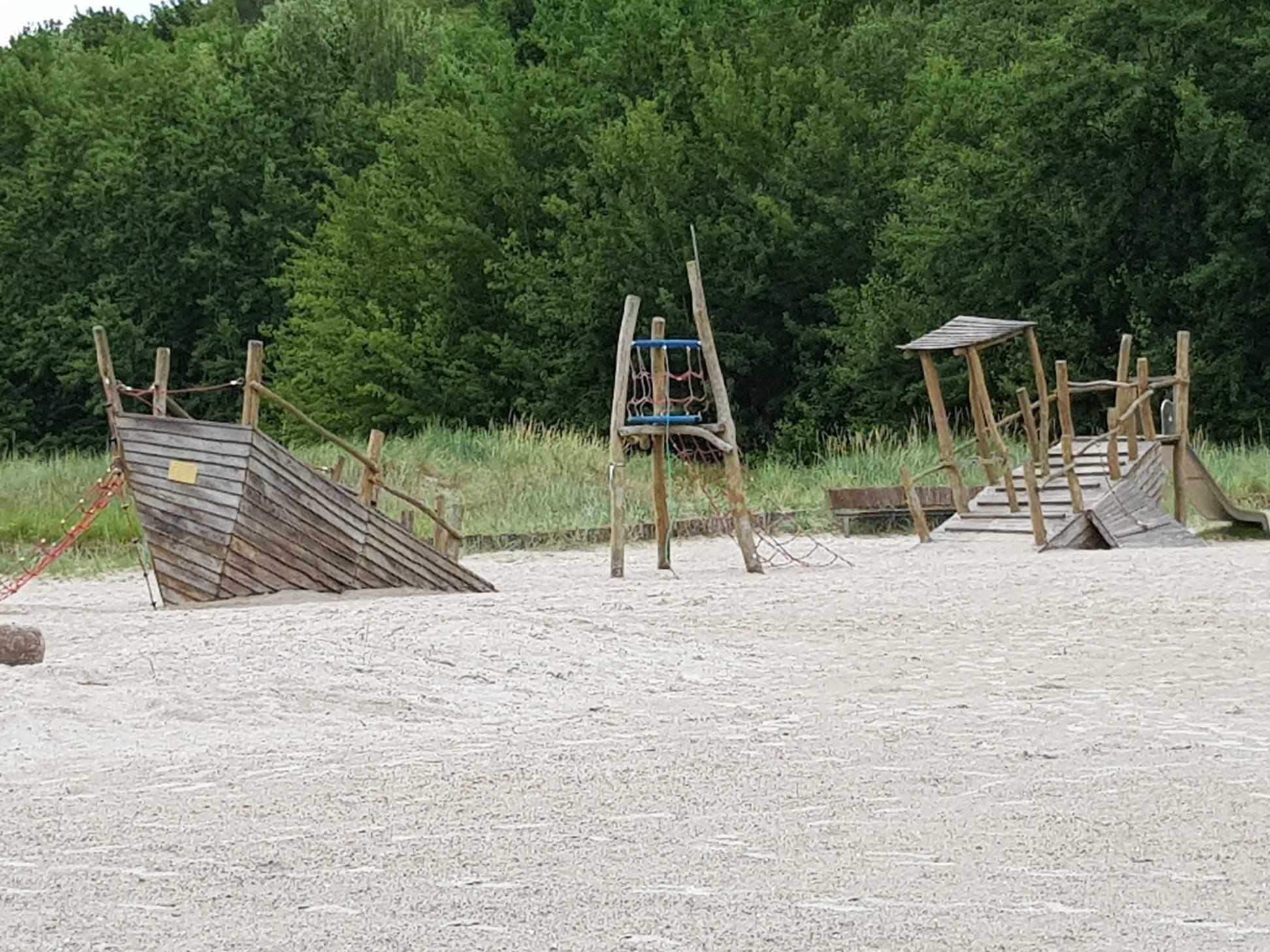 Ein sandiger Strand mit Holzspielgeräten, darunter eine Rutsche und eine Klettergerüst.