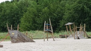 Ein sandiger Strand mit Holzspielgeräten, darunter eine Rutsche und eine Klettergerüst.